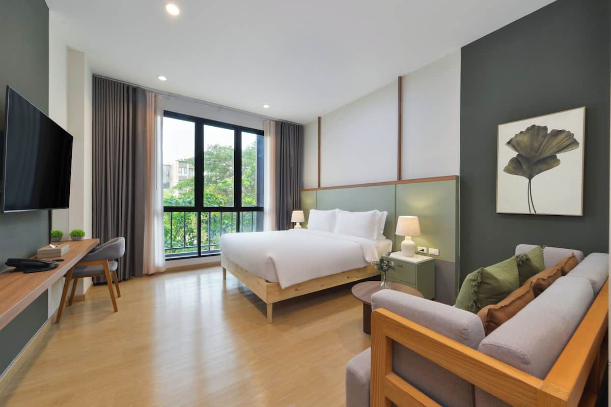 A hotel room with a bed, a desk, a TV, a couch, and a large window.