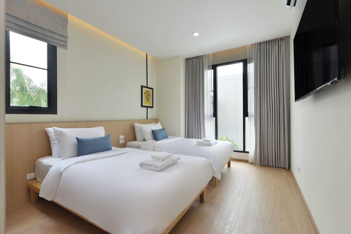 A hotel room with two beds, a flat-screen TV, and a large window with curtains.