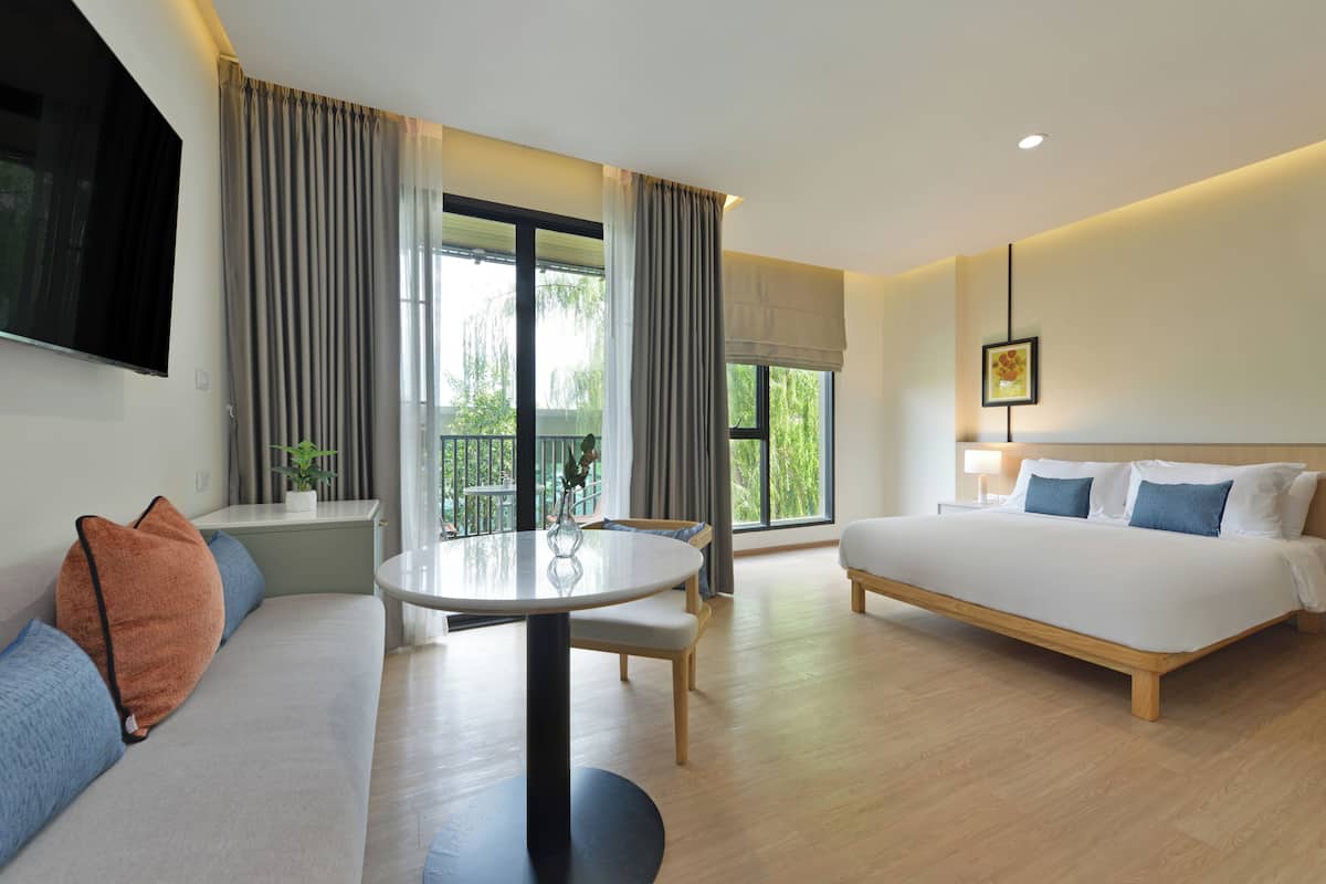 A hotel room with a bed, sofa, dining table, and large windows.