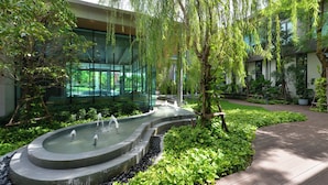 Un giardino tranquillo con una fontana centrale, vegetazione lussureggiante e architettura moderna.