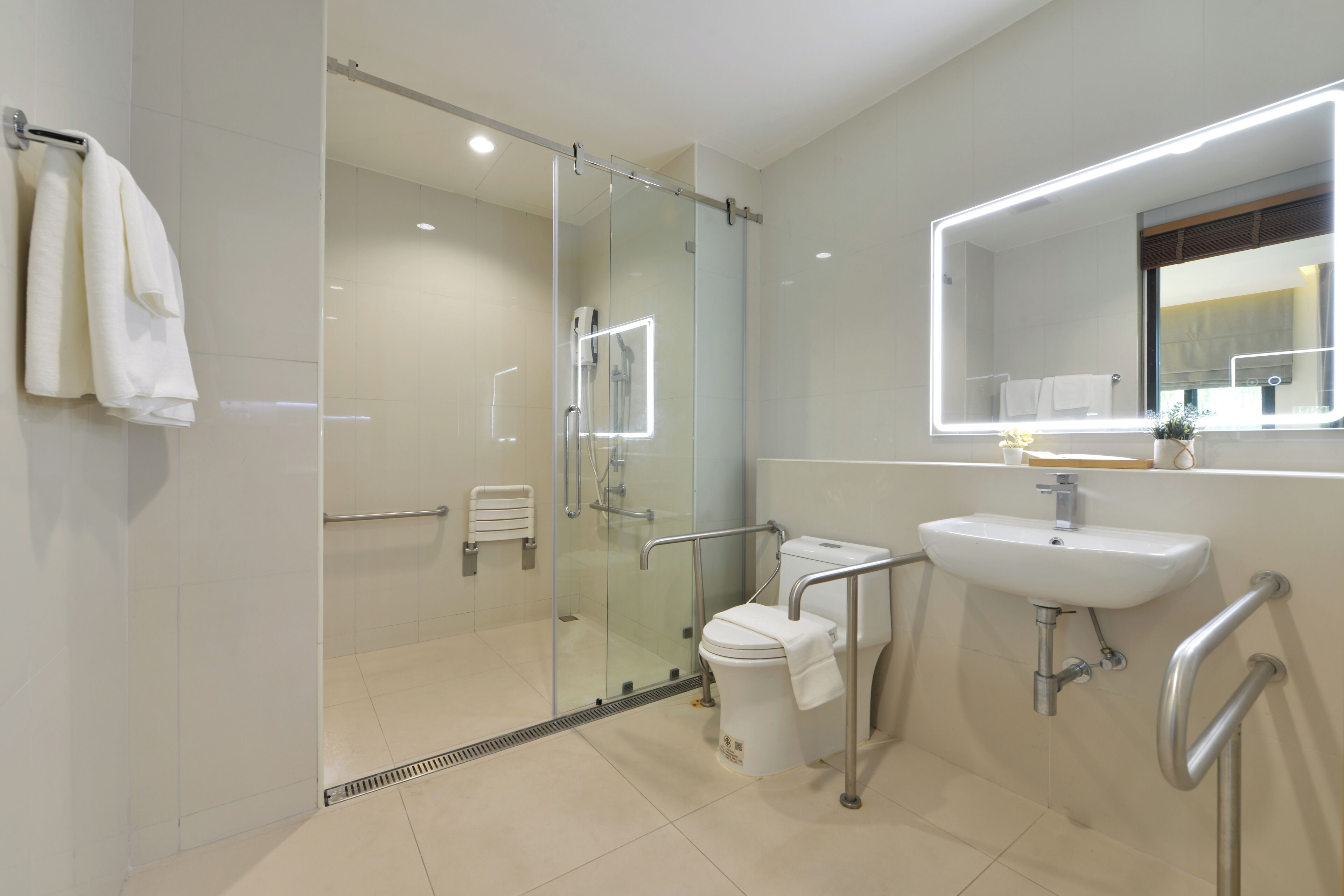 Une salle de bain moderne avec une douche à parois de verre, un lavabo blanc avec un miroir et des barres d’appui.