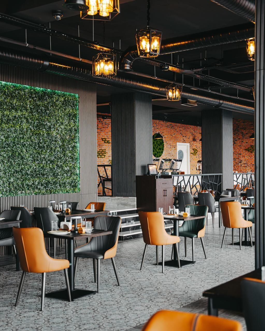 A modern restaurant interior with exposed brick walls, green vertical gardens, and contemporary furniture.