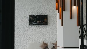 A modern interior with a white textured wall, a mounted TV, a white sofa with cushions, and a decorative light fixture. - Port Marine Hotel By HOLLYWOOD (Baku)