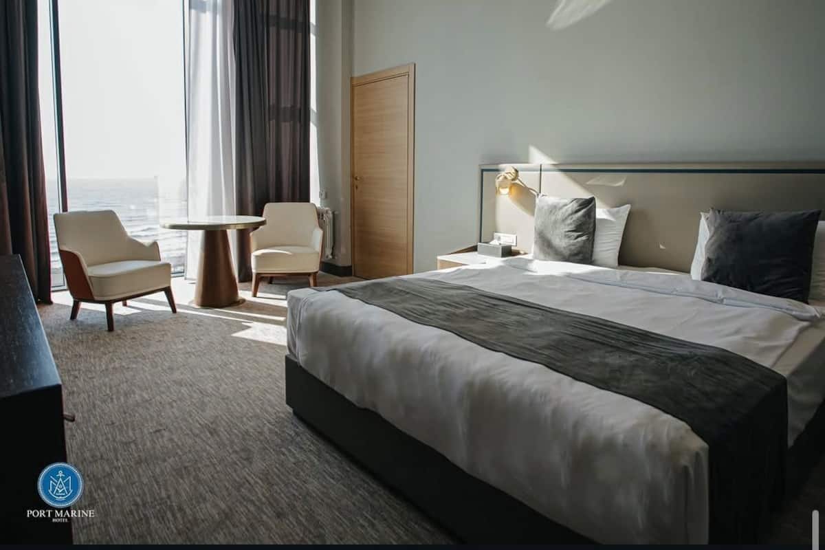 Habitación de hotel con una cama grande, dos sillones, una mesa redonda y vista al océano.