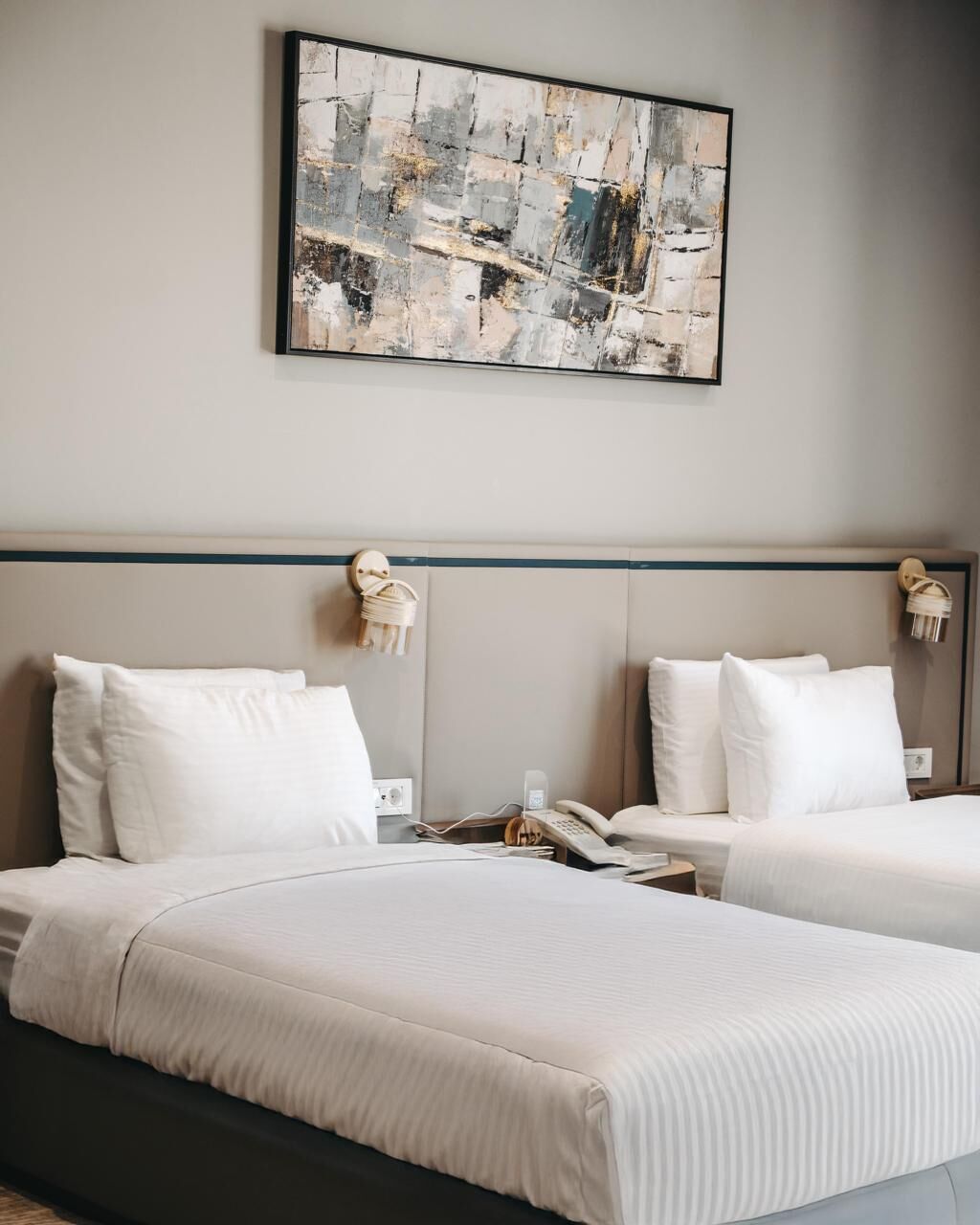 A hotel room with two beds, a cityscape painting, and a wooden wall decoration.