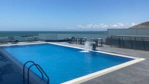 A rooftop pool with a clear view of the ocean, surrounded by lounge chairs and tables. - Port Marine Hotel By HOLLYWOOD (Baku)