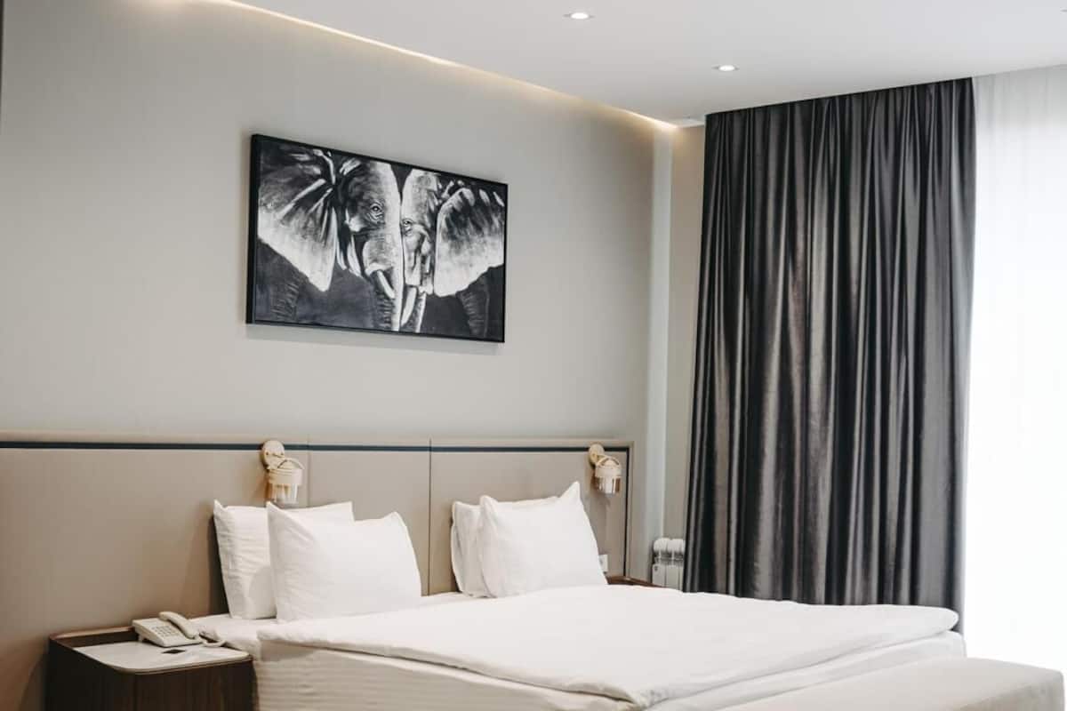 Una habitación de hotel moderna con una cama grande, mesitas de noche, un escritorio y un amplio ventanal con cortinas.