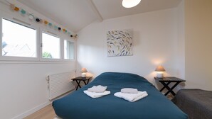 A bedroom with a bed, two bedside tables with lamps, a radiator, and a window with curtains.