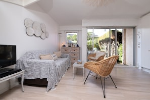 Ein modernes Wohnzimmer mit einer Couch, Fernseher, Korbsessel und Blick durch eine Glastür.