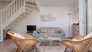 A living room with a staircase, a sofa, two wicker chairs, a coffee table, and a flat-screen TV.