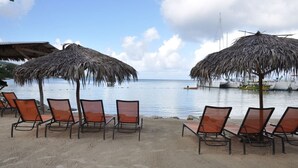 Een strand met rieten parasols en ligstoelen gericht op de zee.