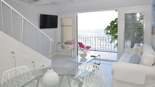 Een moderne woonkamer met een glazen tafel, een witte bank en een balkon met uitzicht op zee.