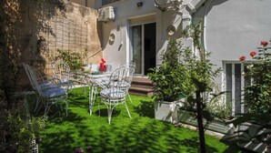 A patio with a table and chairs, surrounded by greenery and a brick wall.