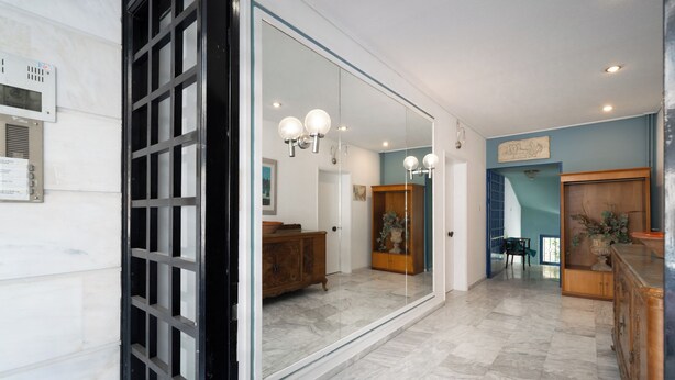 A modern interior with a large mirror reflecting a dining area, a wooden cabinet, and a light fixture.