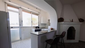 Una cocina moderna con una isla central, dos taburetes de bar, una chimenea y vistas al exterior a través de amplias ventanas.
