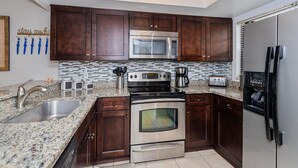 A modern kitchen with dark wooden cabinets, stainless steel appliances, a granite countertop, and a tiled backsplash. - 2BR townhouse w/ pool, hot tub & lazy river (Kissimmee)