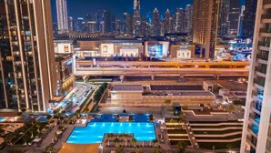 A modern hotel with a large swimming pool, high-rise buildings, and a city skyline in the background.