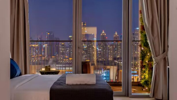 A hotel room with a large window offering a city view at night.