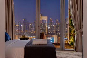 Ein Hotelzimmer mit großem Fenster und Blick auf die beleuchtete Stadt bei Nacht.