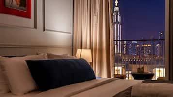 Habitación de hotel con una cama, una mesita de noche, una lámpara y vista a un paisaje urbano nocturno.