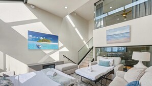 A modern hotel room with a bed, a sofa, a small table, and a painting of a beach scene.