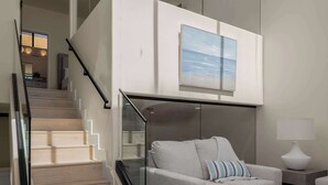 A modern interior with a staircase leading to a loft bedroom, a grey sofa, and a view of the outdoors.