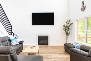Una sala de estar moderna con chimenea, televisor de pantalla plana, sofás de cuero y una mesa de centro de madera.