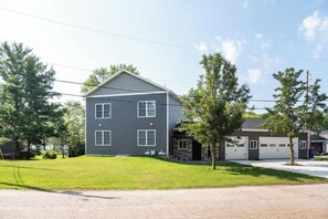 A two-story residential building with a garage, a well-maintained lawn, and trees.