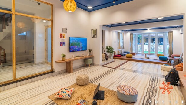 A spacious living area with a large window, a wooden bench, a laptop, and a sofa. - Zostel Chennai Anna Nagar (Chennai)