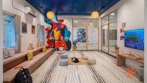 Un moderno vestíbulo de hotel con un mural abstracto lleno de color, una gran pantalla de televisión y un área de descanso con cojines.