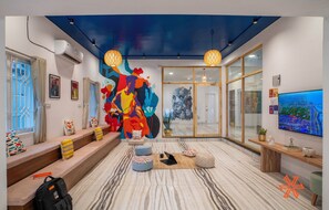Un moderno vestíbulo de hotel con un mural abstracto lleno de color, una gran pantalla de televisión y un área de descanso con cojines.