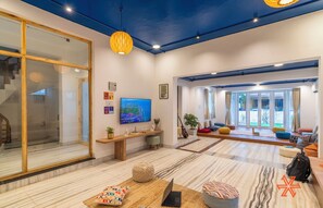A spacious living area with a large window, a wooden bench, a laptop, and a sofa. - Zostel Chennai Anna Nagar (Chennai)