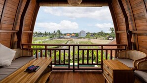 A wooden balcony with a view of a rural landscape, including fields and a distant building. - Villa Aphrodite Ubud (Ubud)