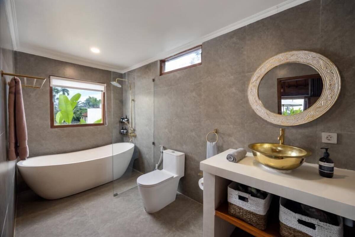 Une salle de bain moderne avec une baignoire sur pieds, des toilettes et un meuble-lavabo doté d’un grand lavabo en laiton.