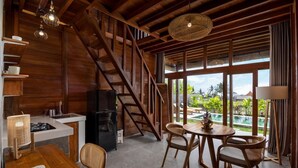 A modern kitchen with a wooden staircase, a dining area with a view of a pool, and a large window. - Villa Aphrodite Ubud (Ubud)