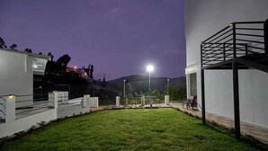 A well-maintained grassy area with a modern building structure, a metal staircase, and a fence. - Darza delite (Ootacamund)