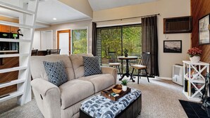 A living room with a beige sofa, patterned cushions, a wooden ladder, a dining area with a table and chairs, and a large window with curtains. - Tanners Ridge 37  with Wintergreen Advantage (Wintergreen)