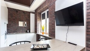 A modern kitchen with a brick wall, a flat-screen TV mounted above the counter, and a tray with glasses and a plant on the table. - Stylish apartments near TSUM (Minsk)