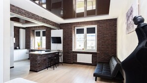 A modern kitchen with a brick backsplash, a dining area with a black sofa, and a large window providing natural light. - Stylish apartments near TSUM (Minsk)