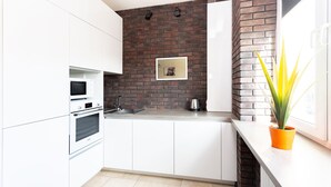 A modern kitchen with white cabinets, a brick accent wall, a stainless steel kettle, and a potted plant. - Stylish apartments near TSUM (Minsk)