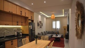 A modern kitchen with wooden cabinets, a dining area with a wooden table and wicker chairs, a living room with a sofa and a coffee table, and a large decorative mirror on the wall. - Casadelmar (Essaouira)