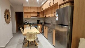 A modern kitchen with wooden cabinets, a stainless steel refrigerator, and a dining area with a table and chairs. - Casadelmar (Essaouira)