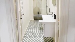 Een smalle gang met een patroon vloer, die leidt naar een badkamer met een wastafel en spiegel.