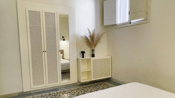Een slaapkamer met een bed, een kast, een radiator en een klein kastje met decoratieve objecten.