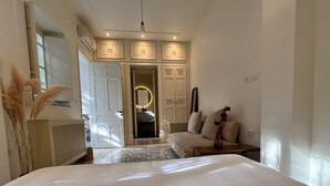 A bedroom with a large bed, a bedside table, a chair, a sofa, a mirror, and a wardrobe.