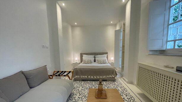 A narrow hotel room with a bed, a sofa, and a small table.