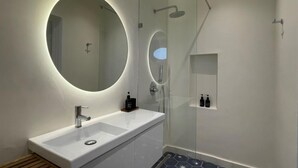 A modern bathroom with a white sink, a large mirror, and a glass-enclosed shower.