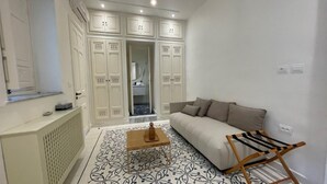 A modern living room with a sofa, a coffee table, and a chair. There is a large window and a door leading to a bathroom.