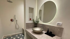 A modern bathroom with a large oval mirror, a vessel sink, a handheld showerhead, and a small plant on the vanity. - Chambre Rabaa   Dar Kbira (Tunis)