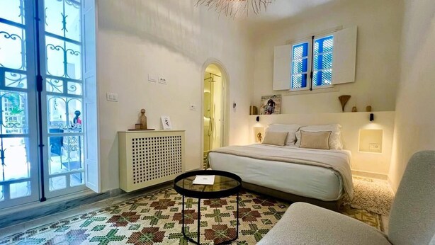 A bedroom with a bed, a round table, a radiator, and a window with a view.